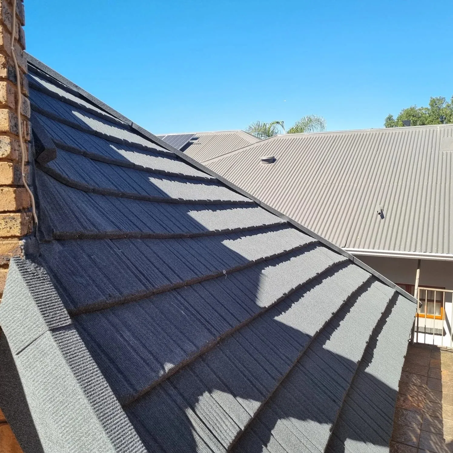 Completed charcoal Harvey tile roof converted from thatch, seen from above against a Highveld blue sky